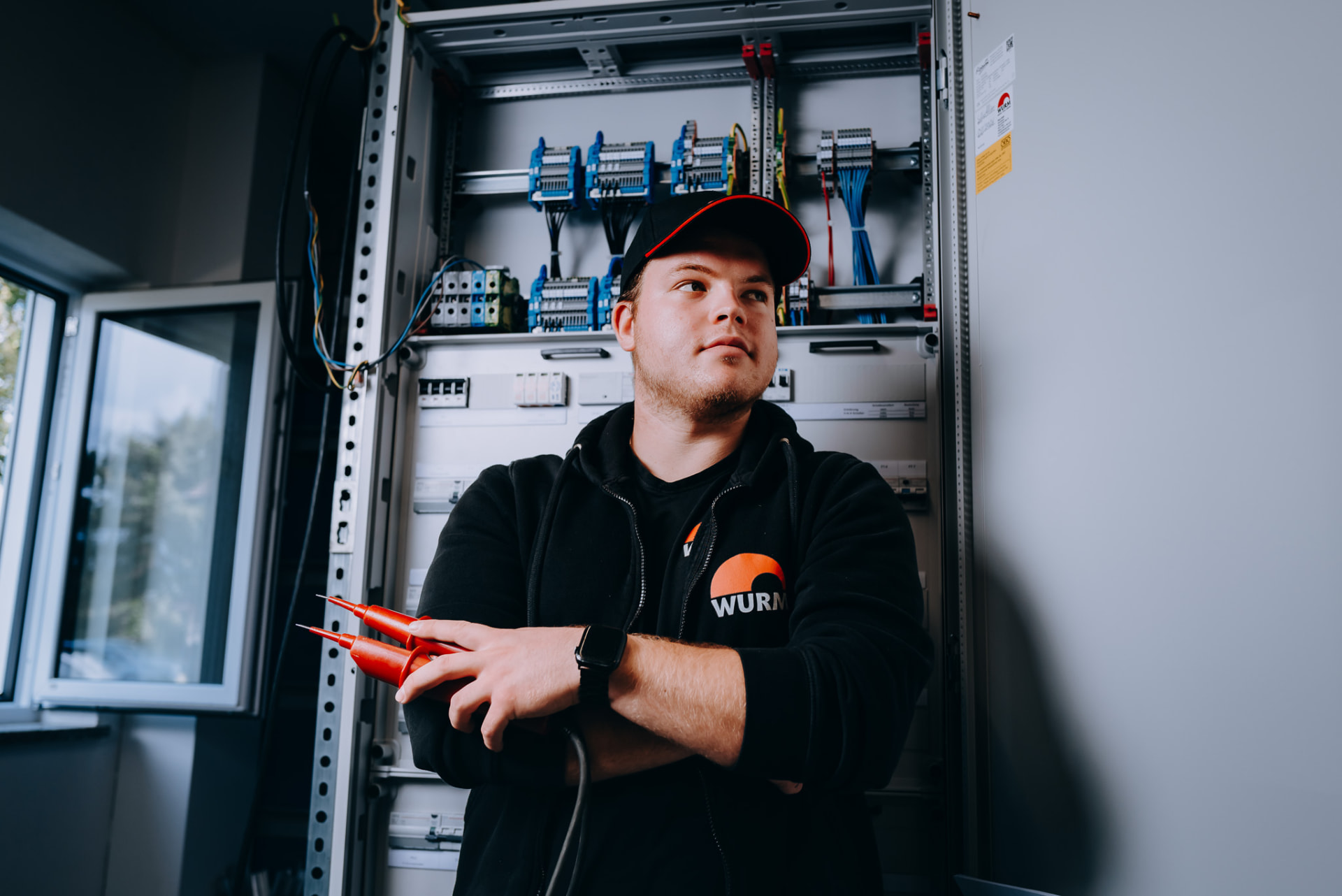 Portrait: Elektroniker mit Prüfspitzen vor Schaltanlage