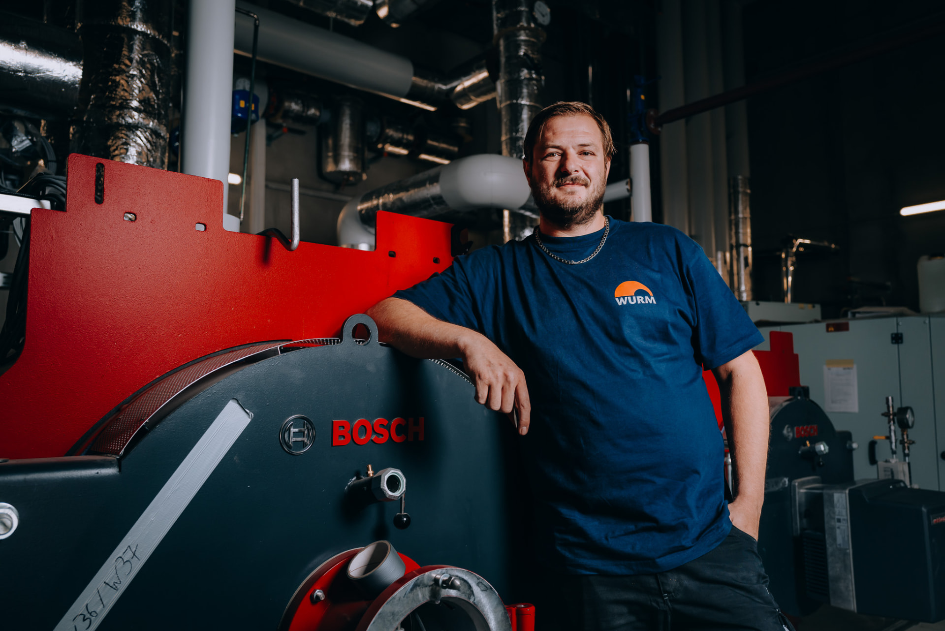 Anlagenmechaniker lehnt am Heizkessel der Energiezentrale
