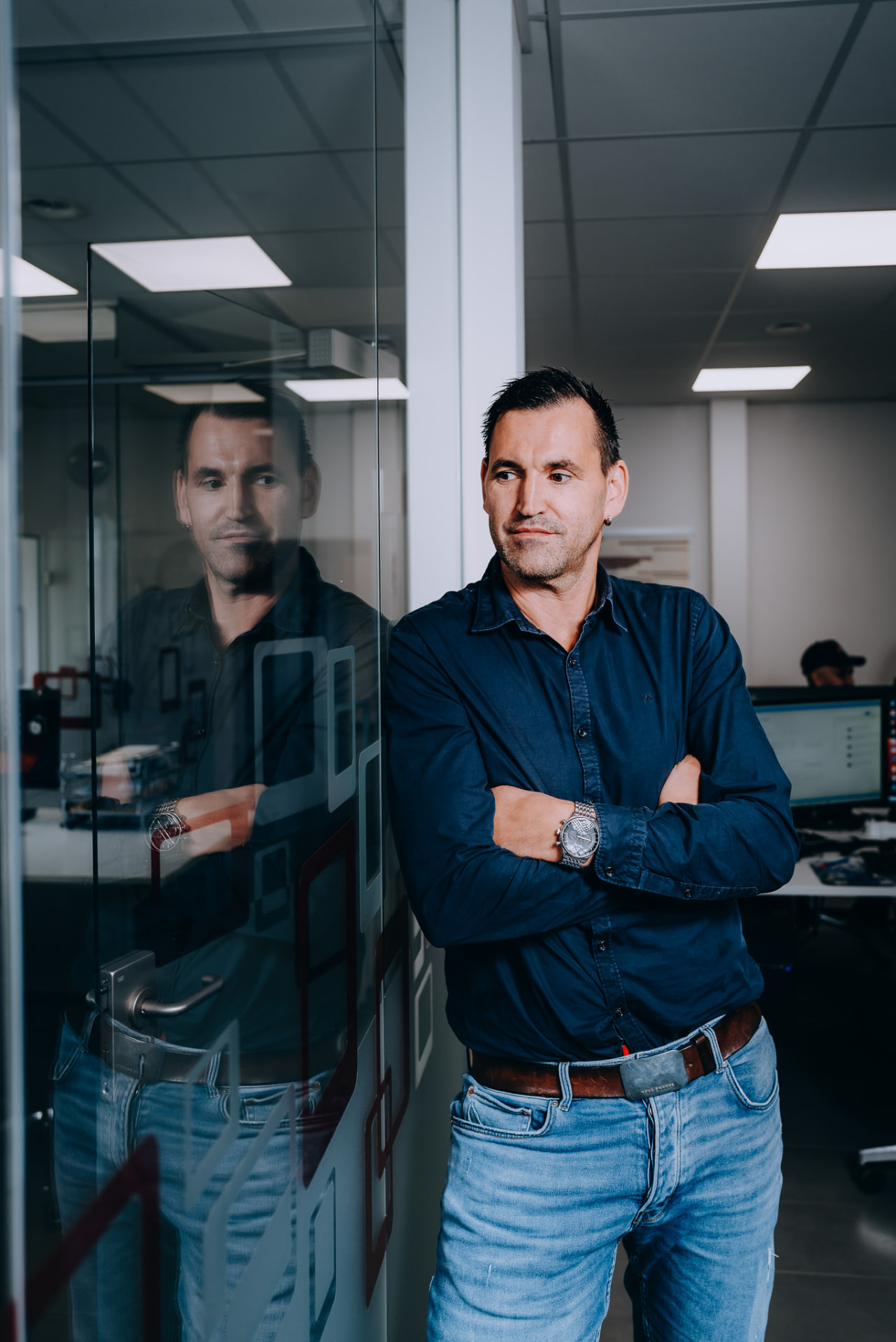 Portrait eines Mitarbeiters mit verschränkten Armen an der Glaswand
