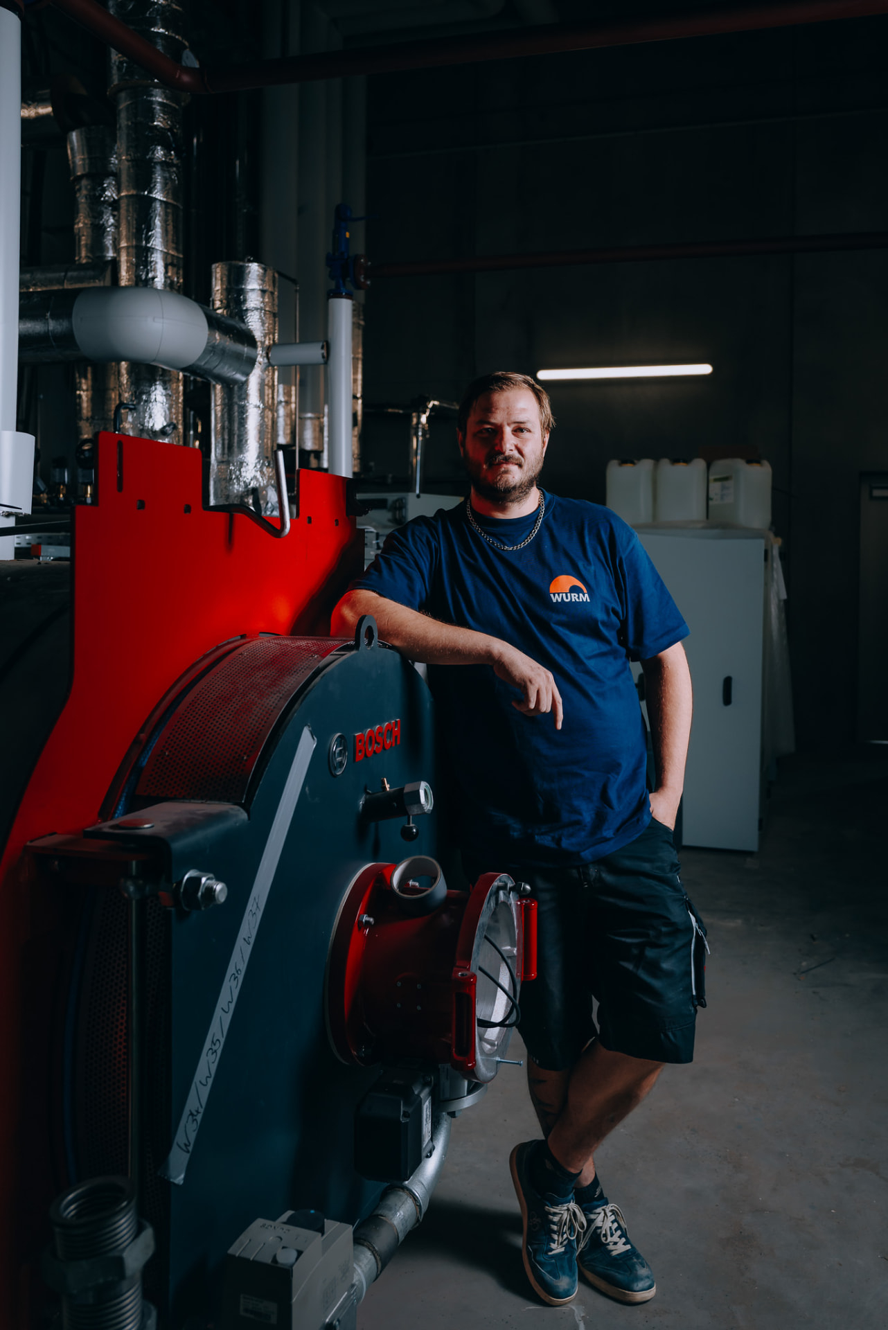Monteur neben Brenner und Kessel im Technikraum, Hochformat