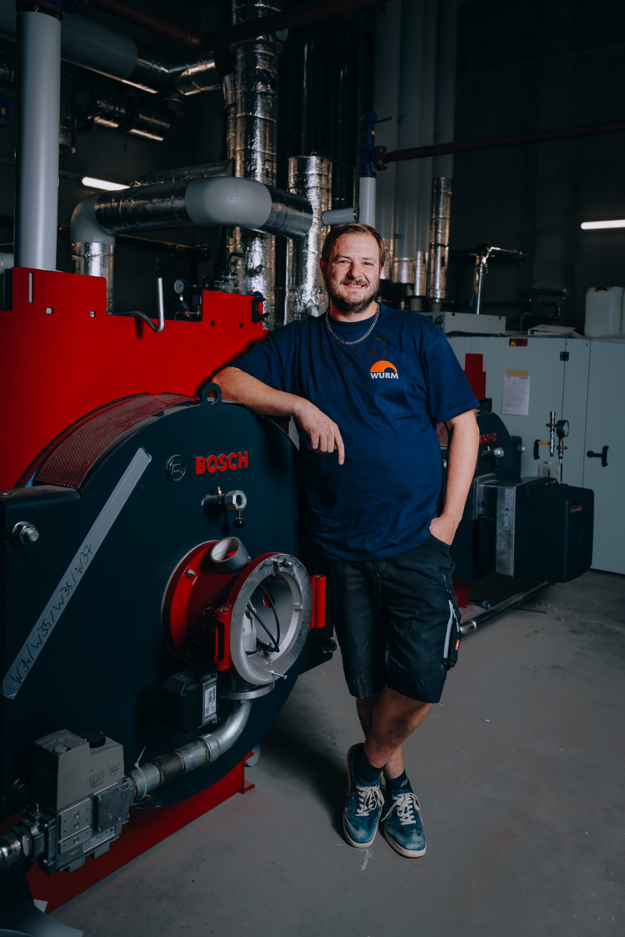 Anlagenmechaniker vor zwei Heizkesseln im Technikraum