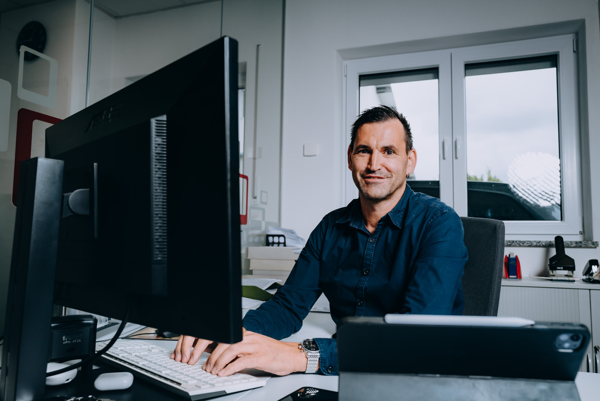 Mitarbeiter am Schreibtisch mit Monitor, Blick in die Kamera