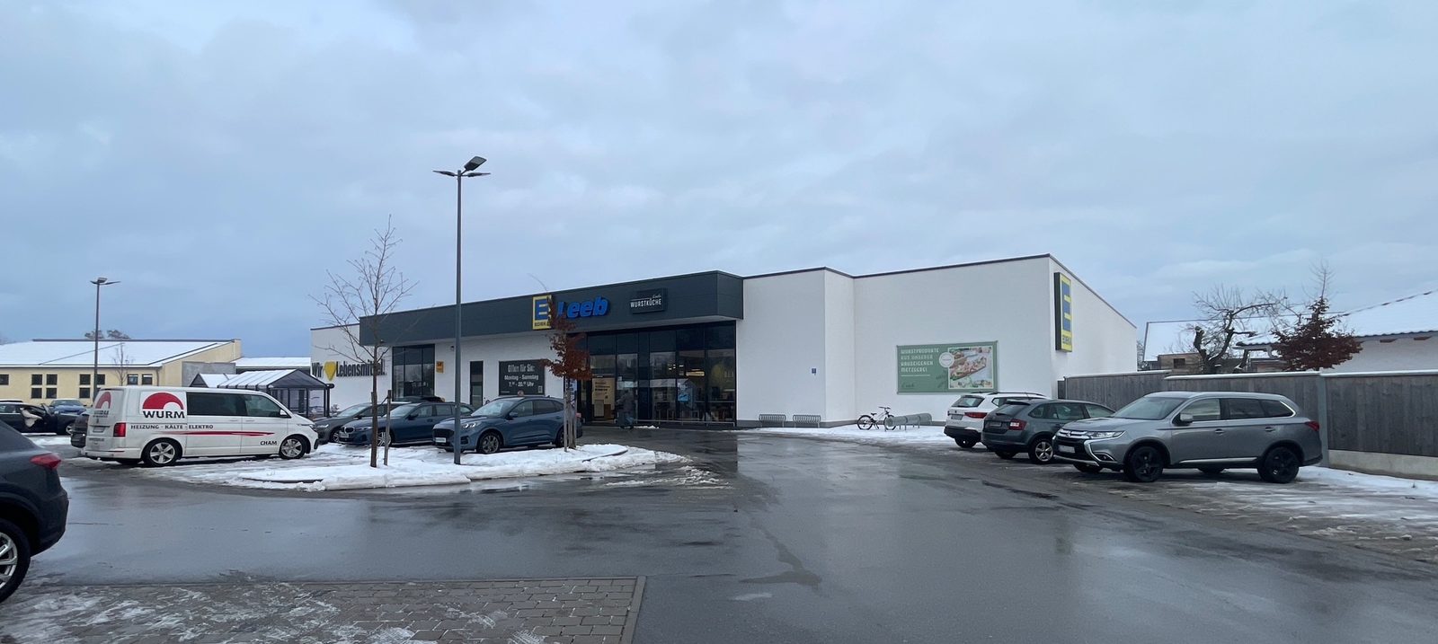 Außenansicht des neu gebauten Edeka-Marktes in Pilsting mit Kundenparkplatz und Montagefahrzeug der Wurm GmbH.