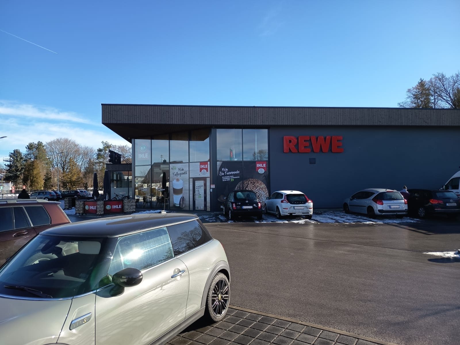 Außenansicht des neu gebauten Rewe-Marktes in Aichach mit Eingangsbereich und Parkplatz.